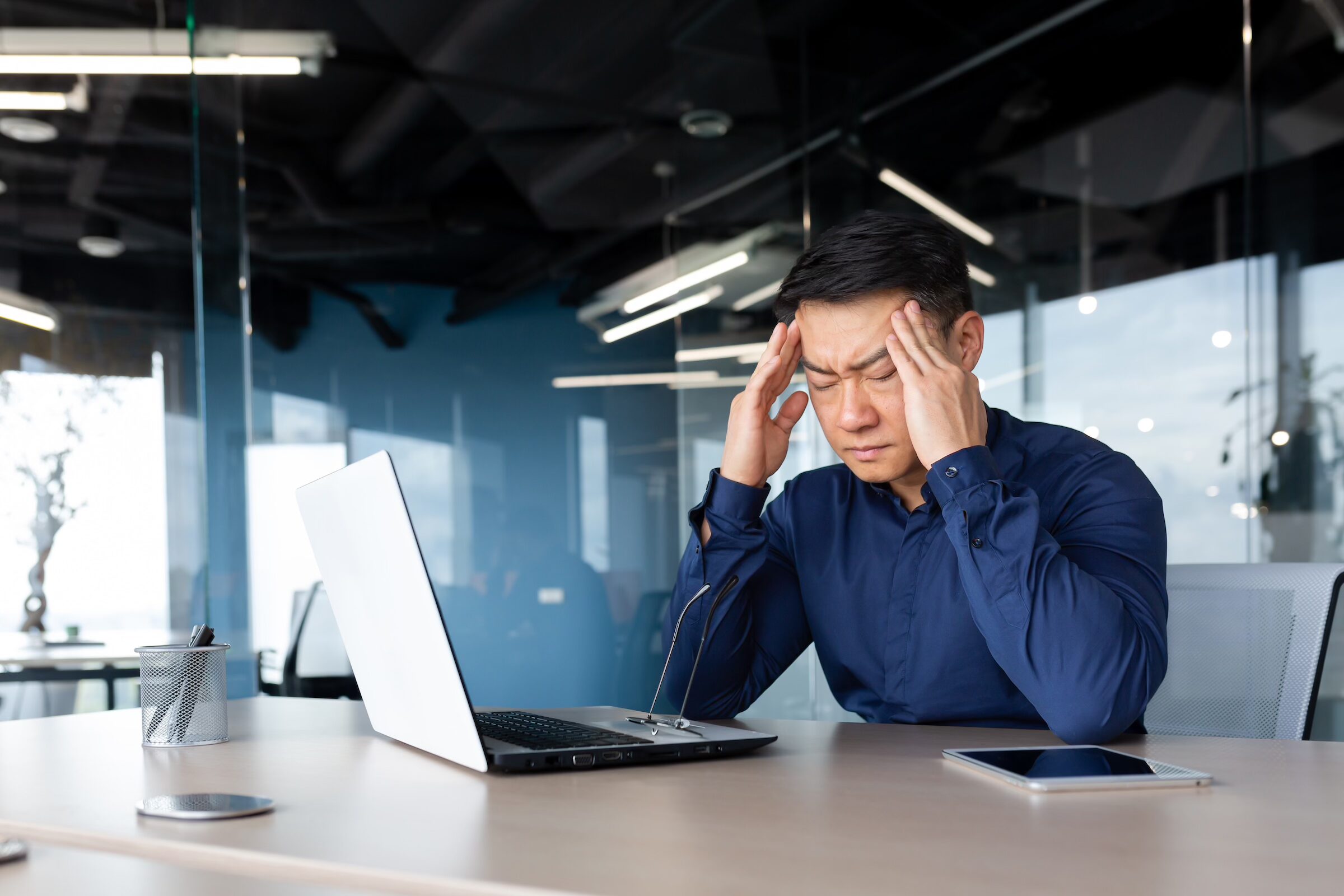 Stressed man at office desk with laptop, illustrating cognitive load and noise distractions.